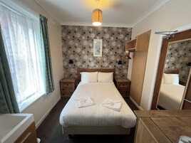 Hotelkamer met een groot bed, twee nachtkastjes, een hanglamp, een spiegel en een raam met gordijnen.