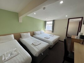 Een hotelkamer met twee bedden, een bureau met stoel en een raam met gordijnen.