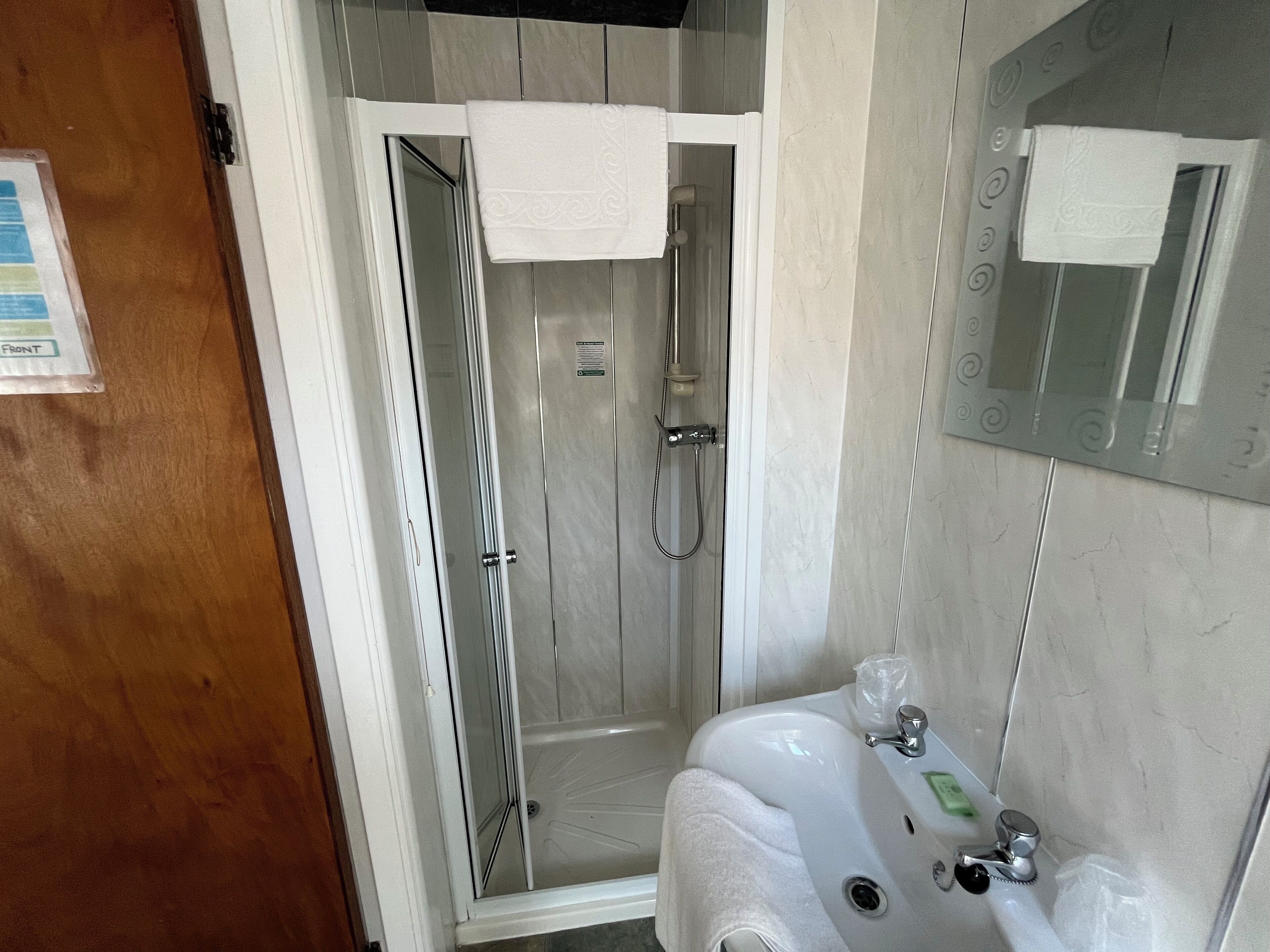 A modern bathroom with a glass-enclosed shower, a sink with a mirror, and a towel hanging on the wall.