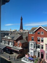 Uitzicht op een stad met een opvallende toren op de achtergrond, woongebouwen met verschillende architectuur en een straat met voetgangers.