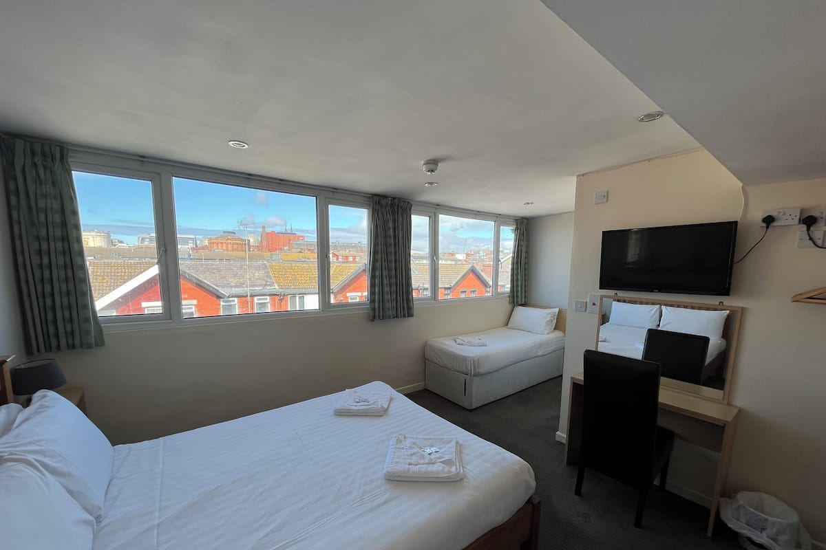 Une chambre d’hôtel équipée d’un lit, d’un bureau, d’une chaise, d’une télévision et d’une fenêtre donnant sur la ville.