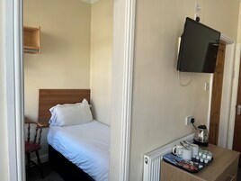 Hotelkamer met een bed, een houten stoel, een aan de muur bevestigde televisie, een radiator en een tafel met waterkoker en kopjes.
