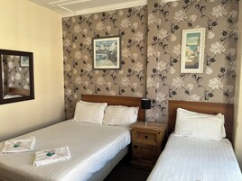 Een hotelkamer met twee bedden, bloemenbehang en ingelijste foto's aan de muur.