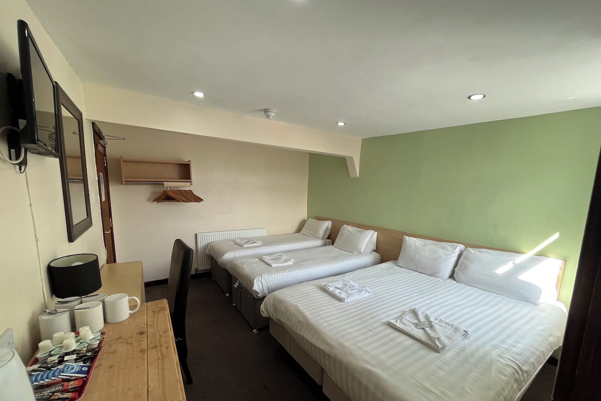 Une chambre d’hôtel avec deux lits simples, un bureau en bois avec une machine à café, un miroir et un radiateur.