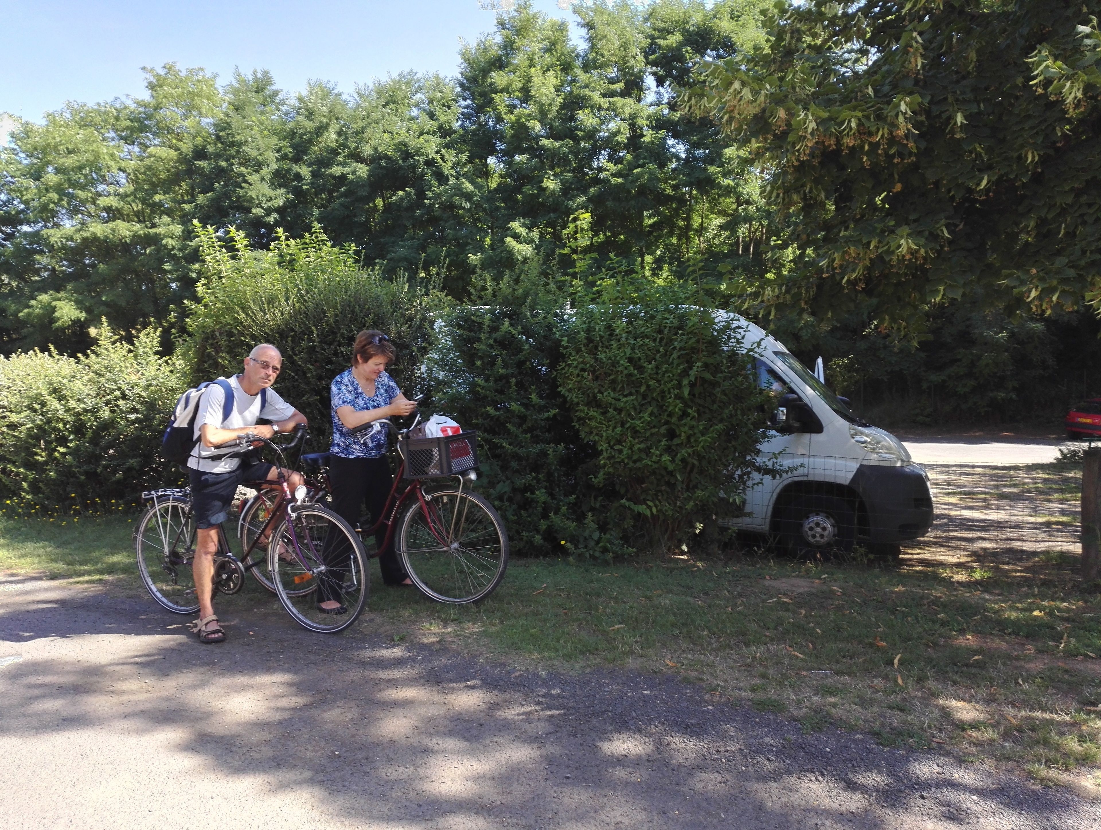 Two people standing beside bicycles, with a white vehicle parked nearby.
