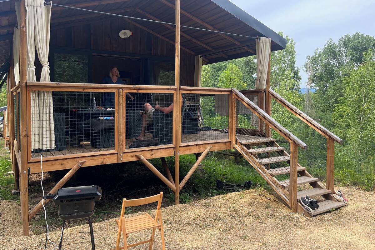 A wooden deck with a covered area, a chair, and a grill.