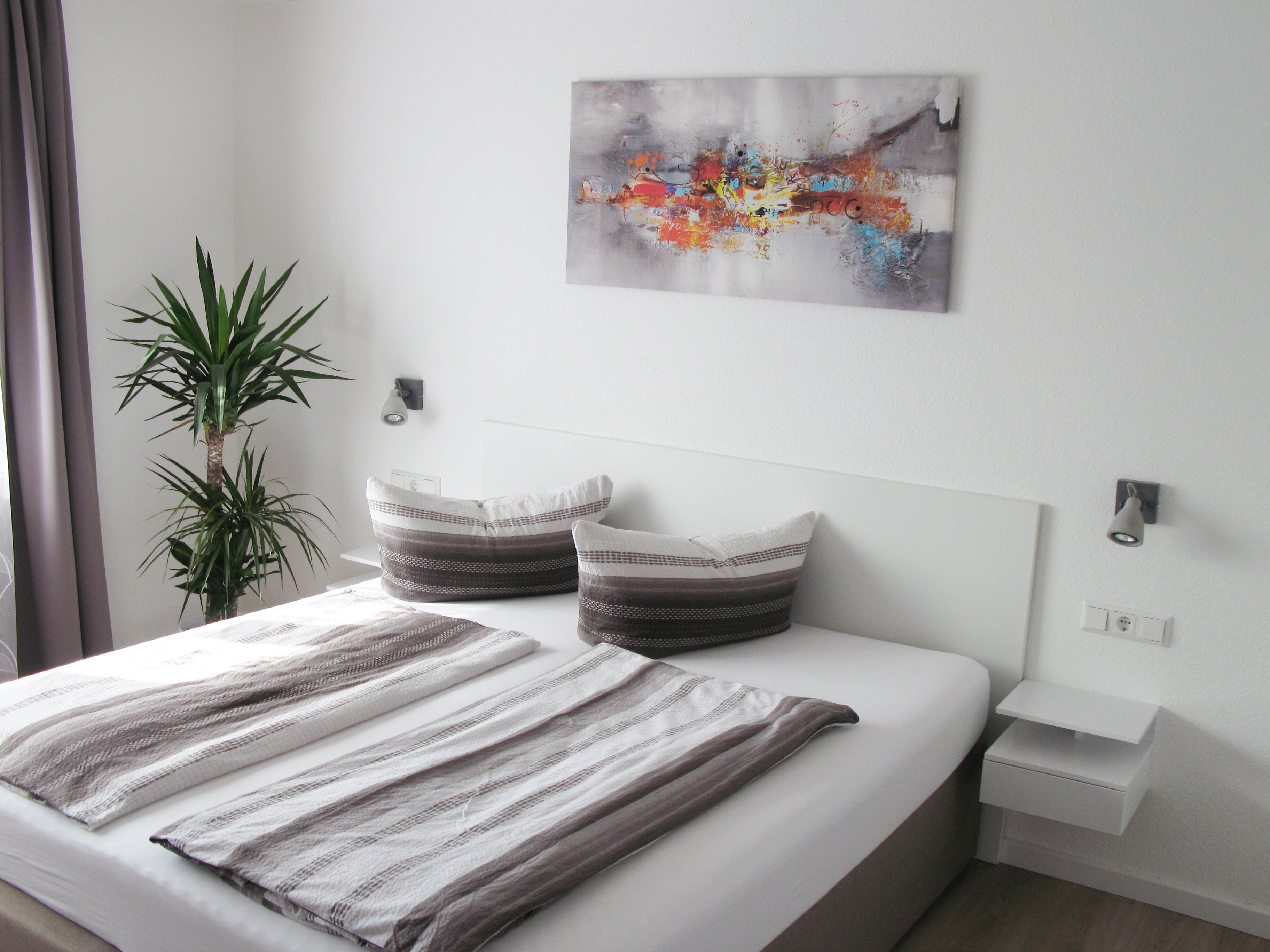 A neatly made bed with striped bedding, a modern headboard, and a small bedside table with a lamp.