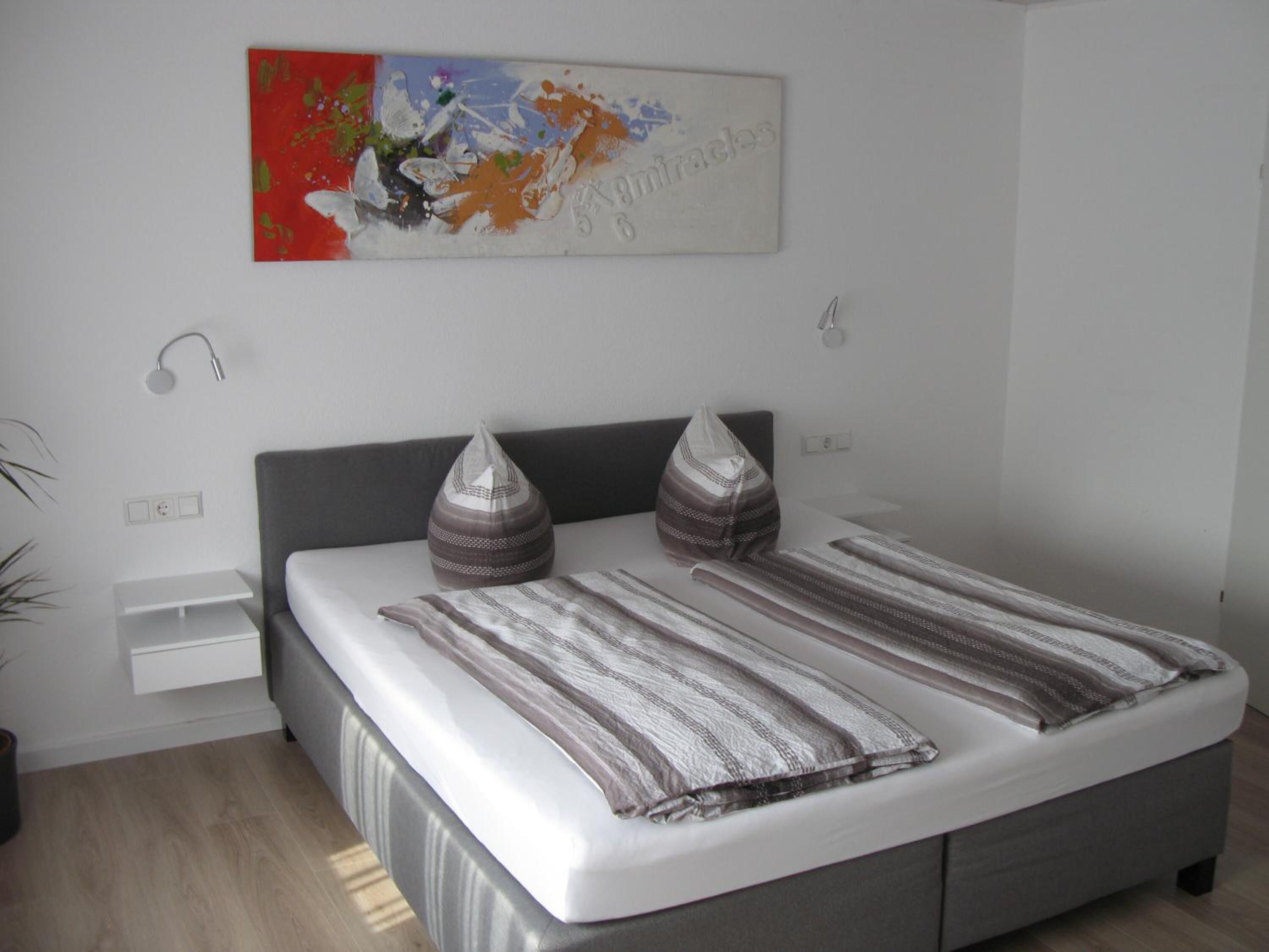 A modern bedroom with a bed, bedside tables, and a wall-mounted artwork.