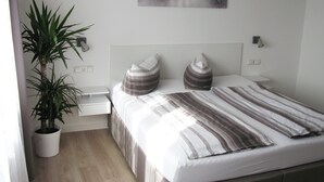 Un dormitorio ordenado con cama, mesitas de noche, una planta en maceta y una obra de arte en la pared.