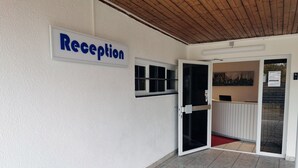Zona de recepción con un cartel que dice 'Recepción' y una puerta de vidrio que da al interior.