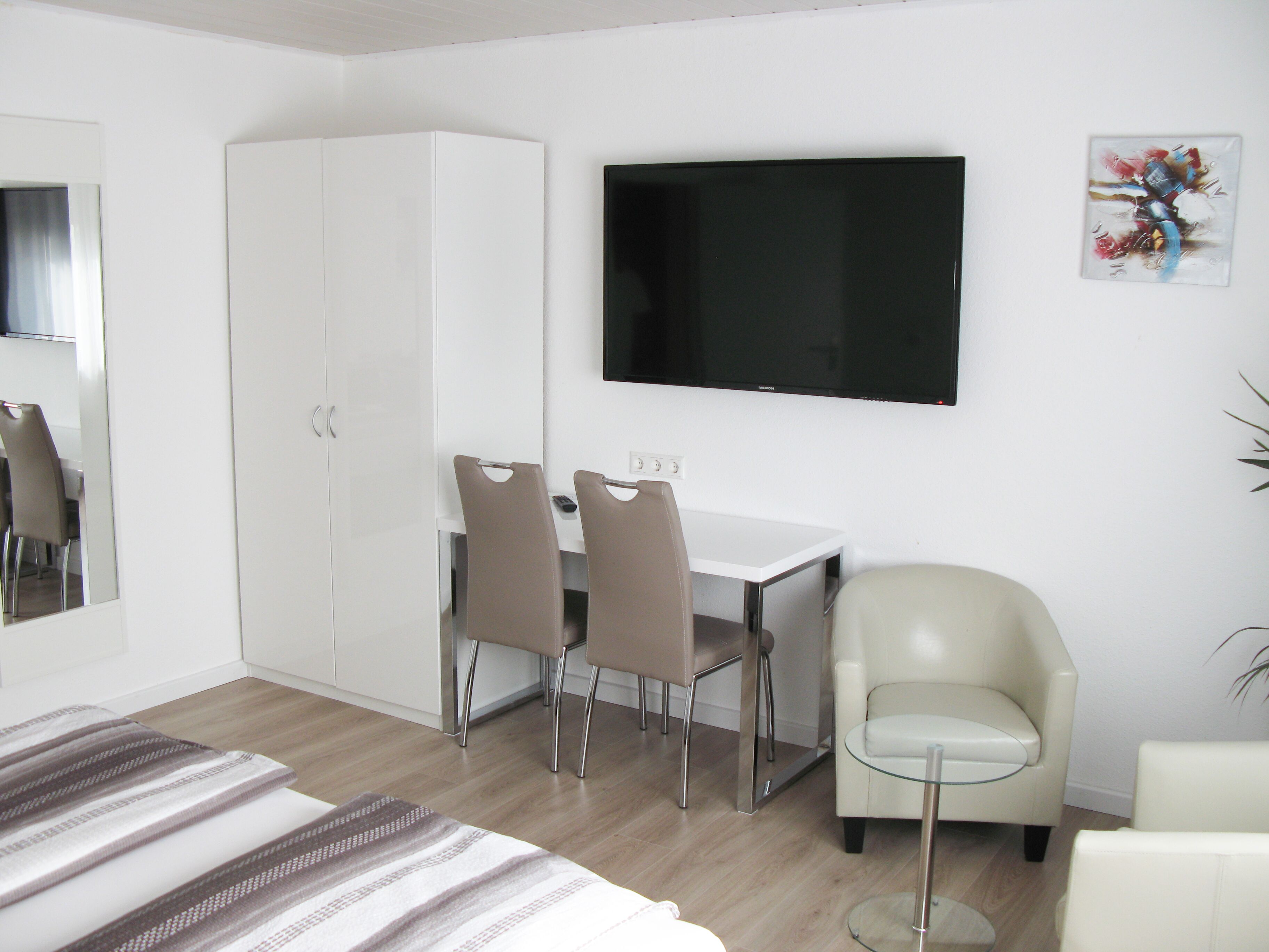 A modern hotel room with a bed, a desk with two chairs, a TV, and a glass coffee table.
