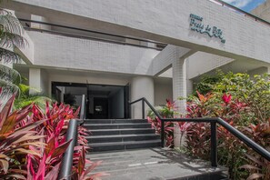 A building entrance with a staircase leading up to a door, surrounded by tropical plants. - PIP201 Cozy flat in Boa Viagem 4 people. (Recife)