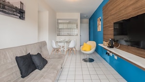En moderne stue med en beige sofa, et spisebord med stole og et køkkenområde med en blå accentvæg.