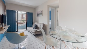 En moderne stue med en sofa, et glasbord med plads til fire personer og en balkon med blå gardiner.