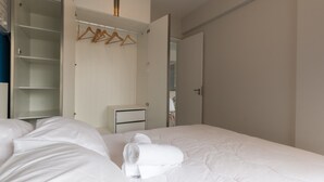 Et hotelværelse med en pænt redt seng, en garderobe med bøjler og et lille natbord.