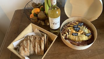 Une table en bois sur laquelle se trouvent une bouteille de vin, un bol de fromage et de noix, un panier de fruits et une miche de pain.