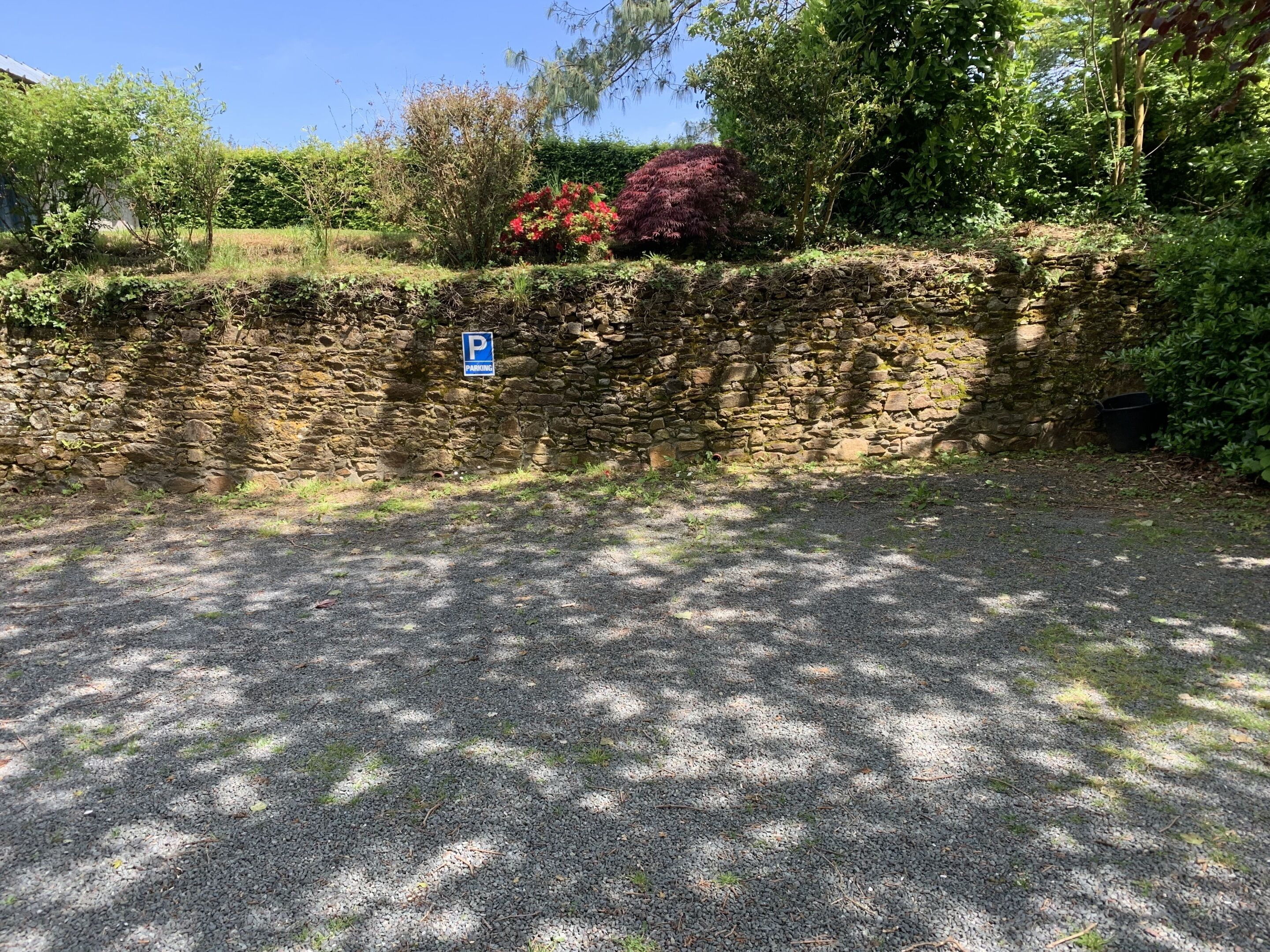 A gravel parking area with a stone wall and a blue parking sign.