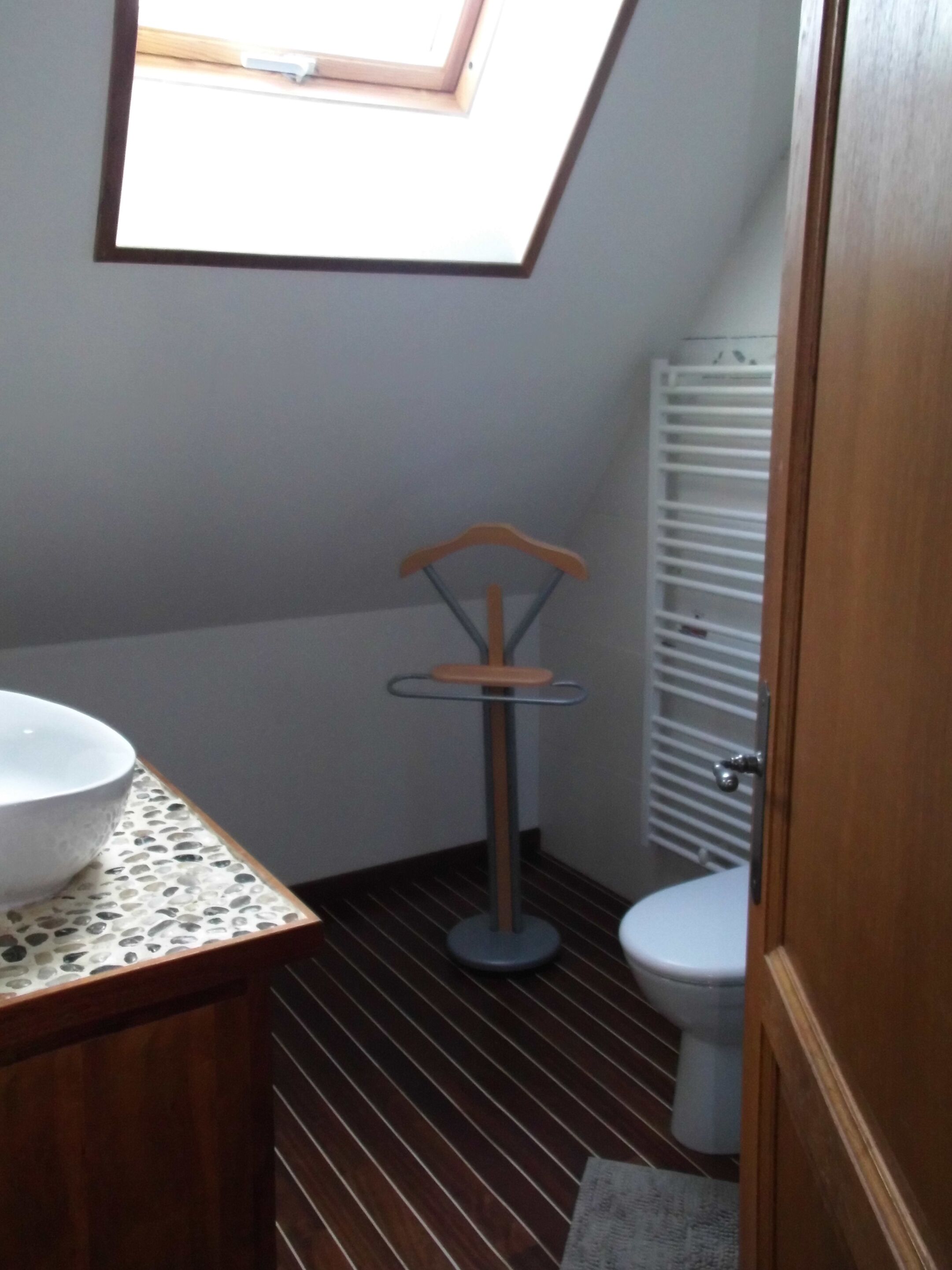 Une salle de bain avec un puits de lumière, une chaise en bois, un lavabo blanc et des toilettes.