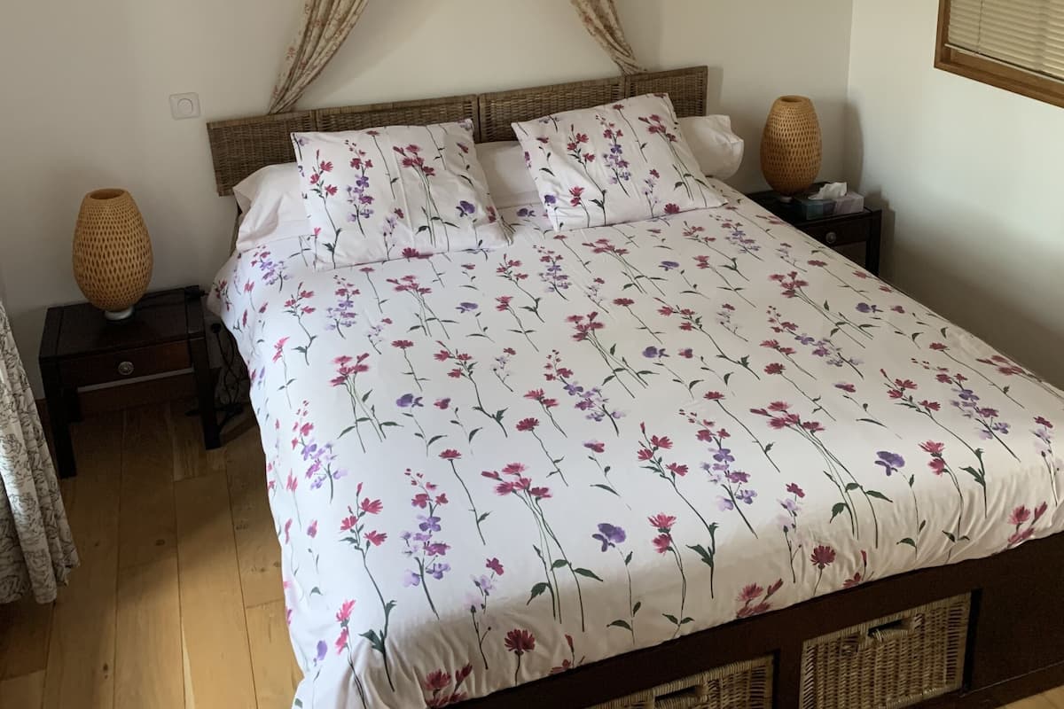 Una cama bien hecha con ropa de cama floral, cabecera de madera y lámpara colgante.