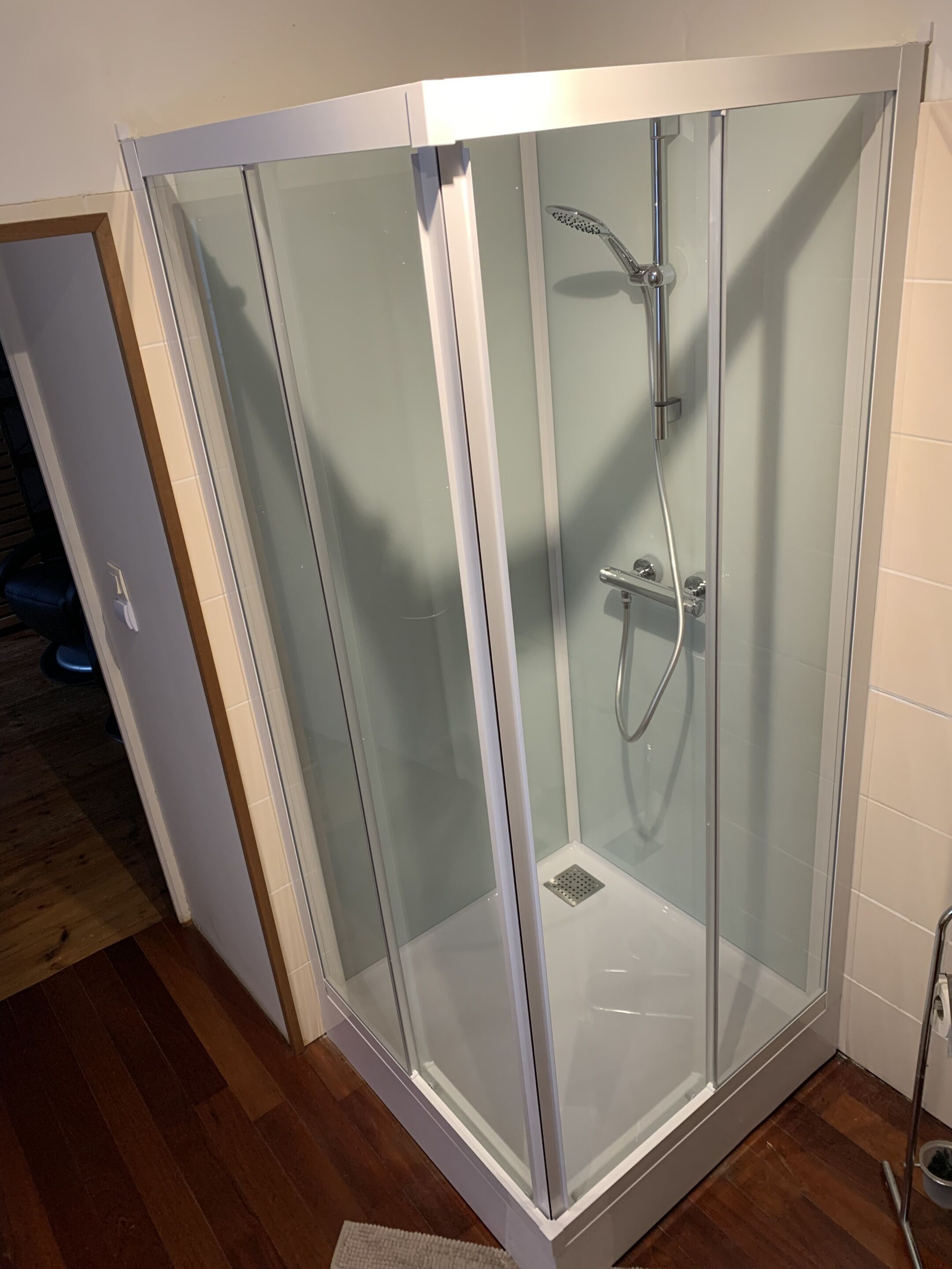 A glass-enclosed shower area with a handheld showerhead and a wall-mounted faucet.