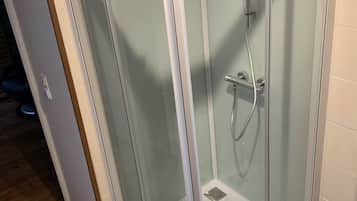 A glass-enclosed shower area with a handheld showerhead and a wall-mounted faucet.