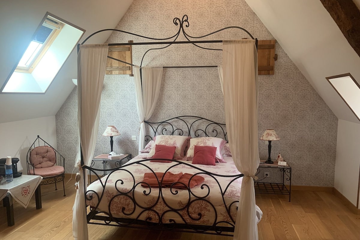 Una cama con dosel en una habitación con techo inclinado y tragaluz.