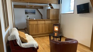 Una sala acogedora con un sofá de cuero rojo, un sillón de cuero marrón, una mesita redonda y una estufa de leña.