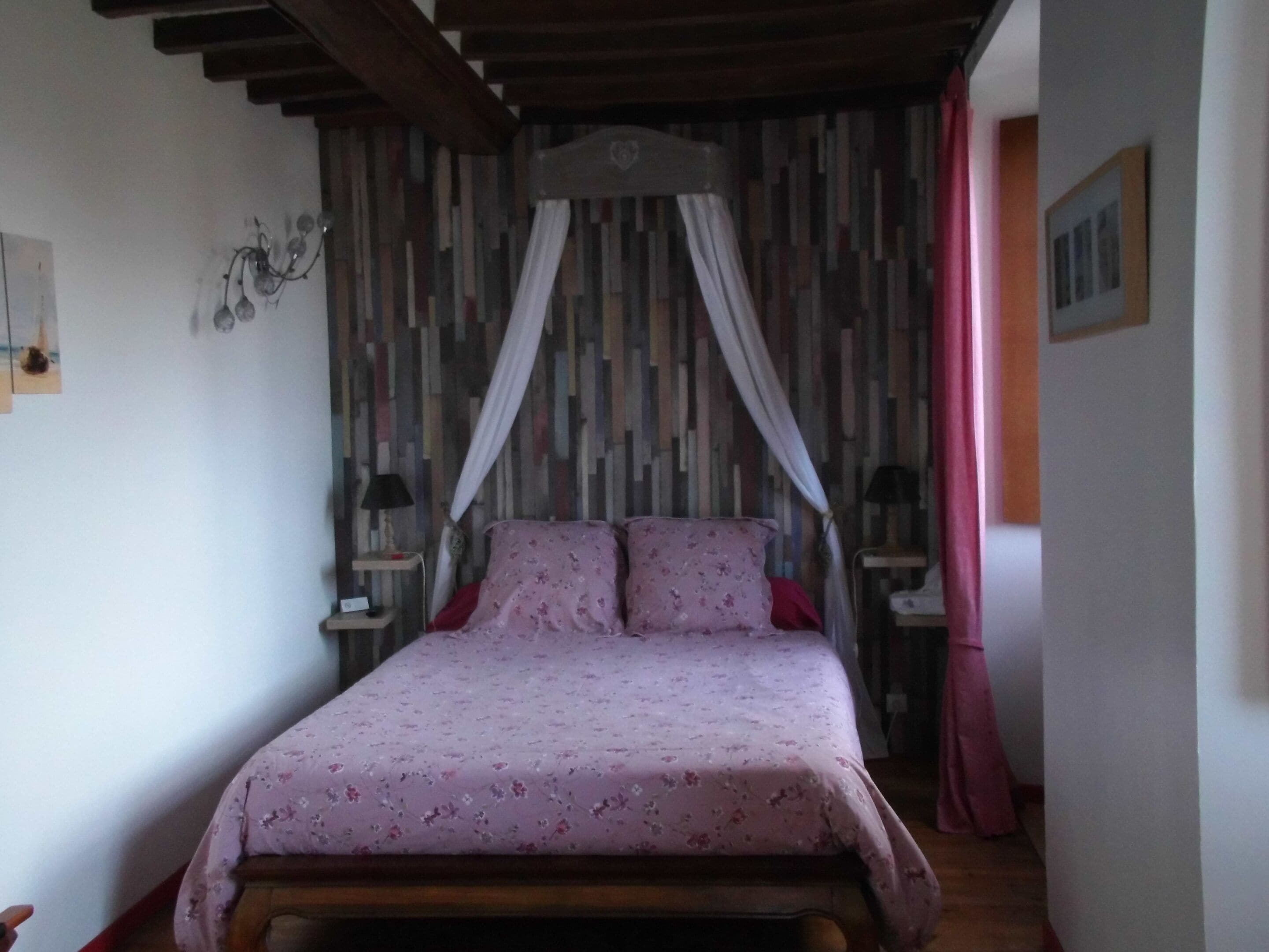 A bedroom with a wooden bed, floral bedding, a canopy, and a striped wall.
