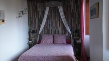A bedroom with a wooden bed, floral bedding, a canopy, and a striped wall.