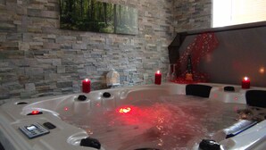 Un jacuzzi con velas rojas, un control remoto y una pared de piedra con una pintura de un bosque.