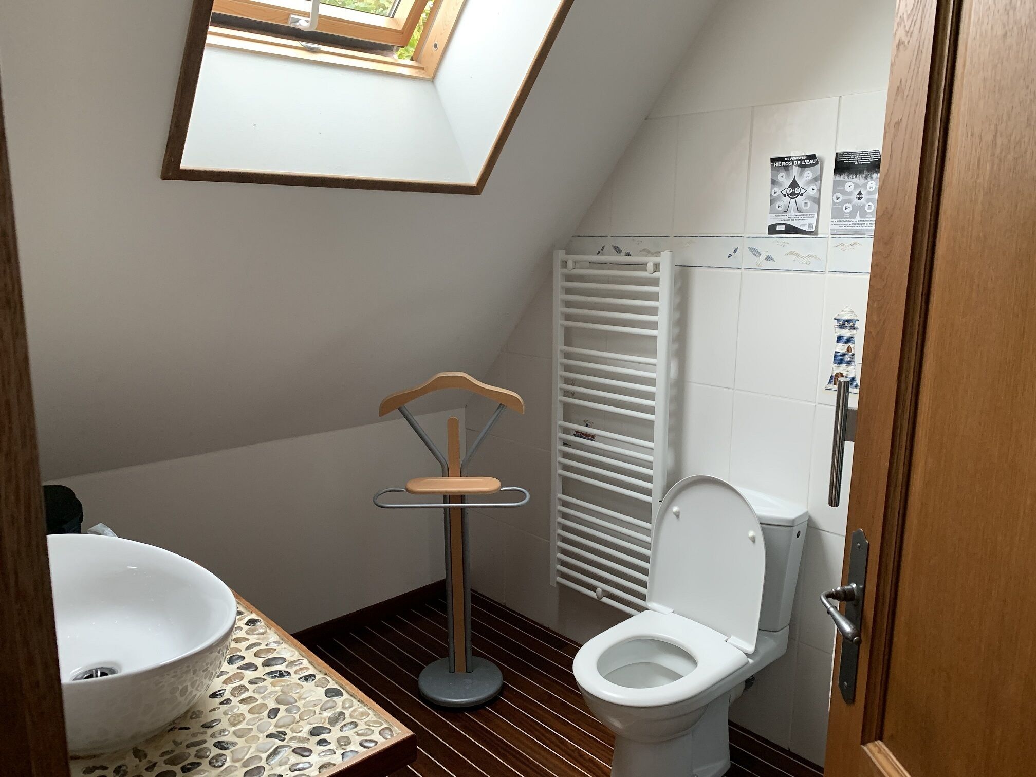 A small, compact bathroom with a skylight, a white sink, a toilet, and a towel rack.