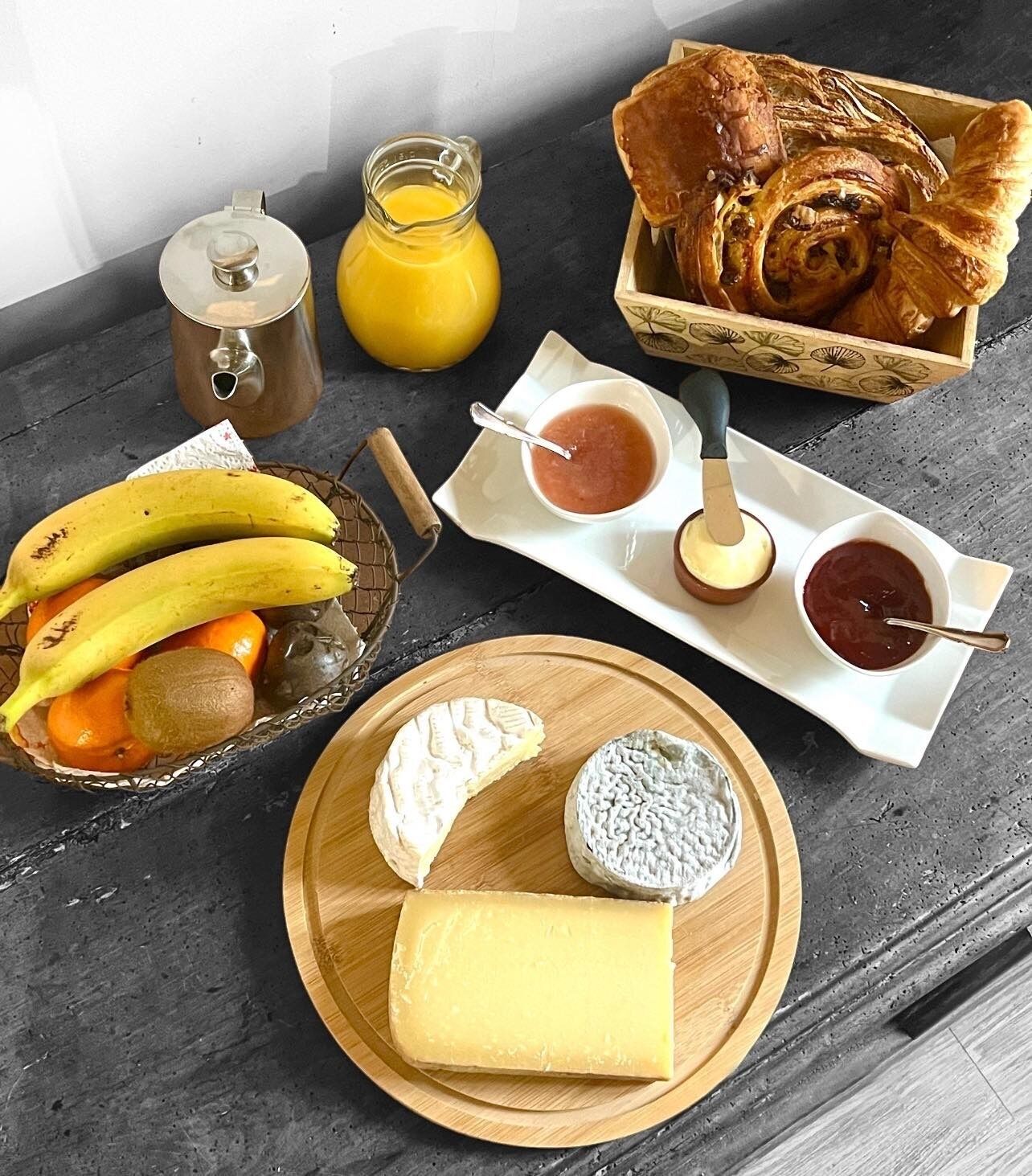 A breakfast setting with various food items including bananas, oranges, cheese, and pastries.