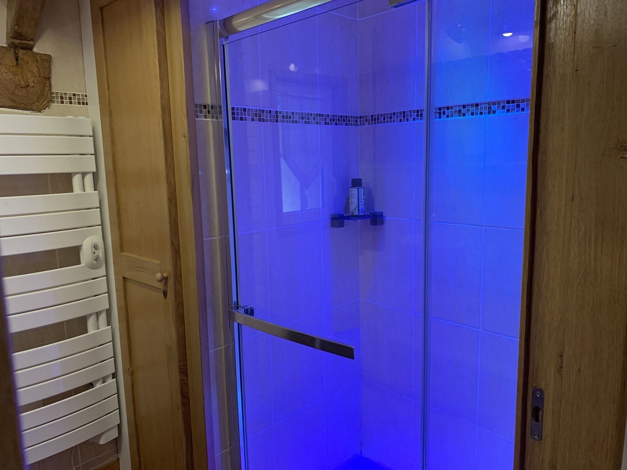 A glass-enclosed shower with a tiled wall and a wooden door frame.