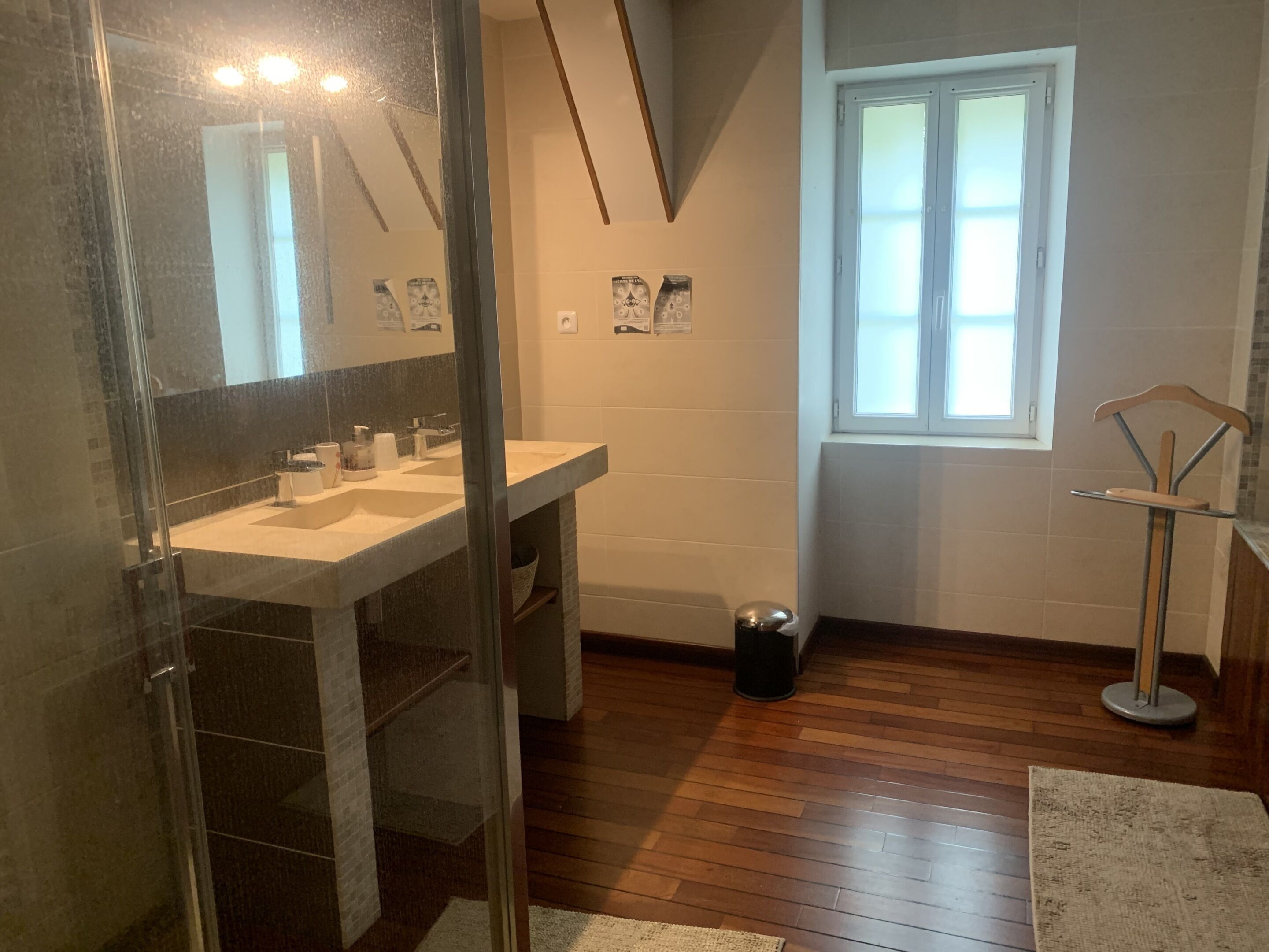 A bathroom with a glass shower enclosure, a sink with a mirror, and a window.