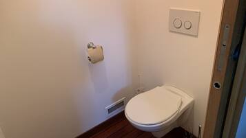 Ein kleines, sauberes Badezimmer mit Toilette, Papierhalter, Lüftung und Lichtschalter an der Wand.