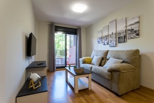 Una sala de estar moderna con sofá, una mesa de centro, televisor y balcón con vistas a zonas verdes.