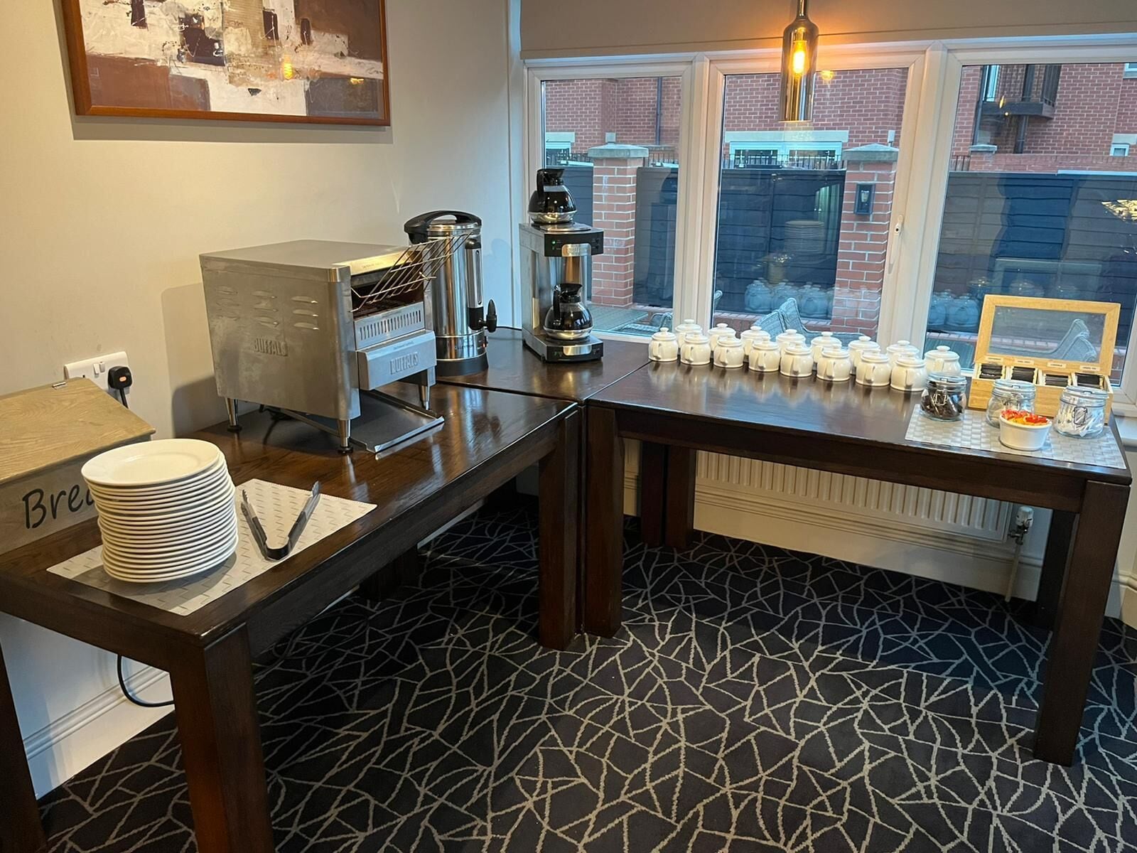 Una zona de cocina con una cafetera, una pila de platos y una mesa con salsas y aderezos.