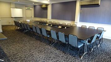 Une salle de conférence avec une longue table et des chaises, un sol recouvert de moquette et un climatiseur fixé au mur.