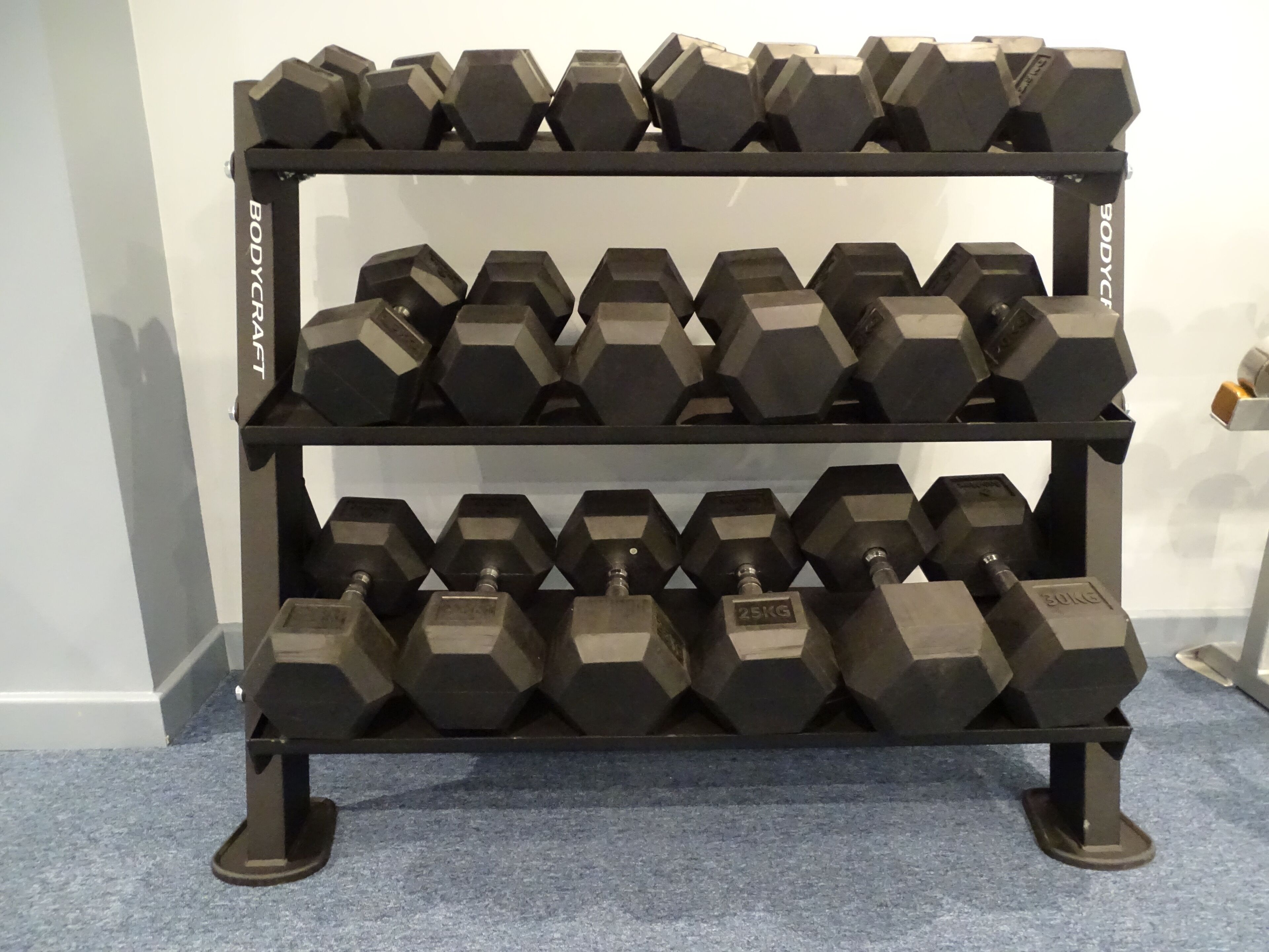 A rack of hexagonal dumbbells with weight markings, arranged on a stand.
