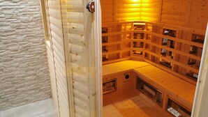 Una sauna con paredes y bancos de madera, una pared de piedra adyacente a la sauna, y una puerta con manija.
