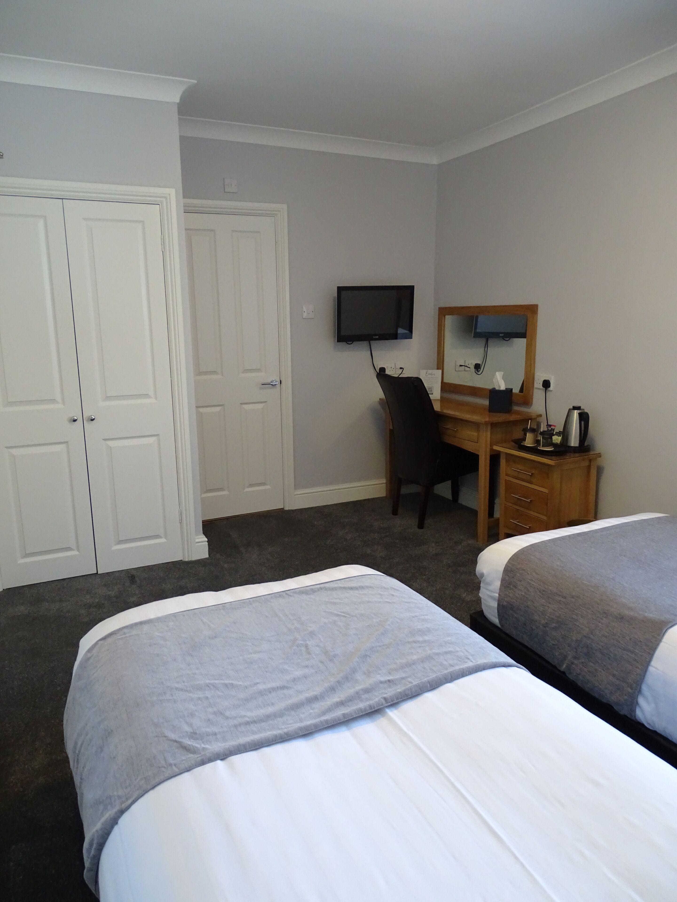 A hotel room with two beds, a desk with a chair, a television, and a wardrobe.