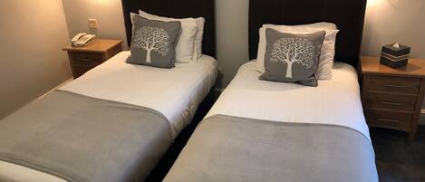 Two twin beds with matching headboards and bedside tables, each with a lamp, a phone, and a tissue box.