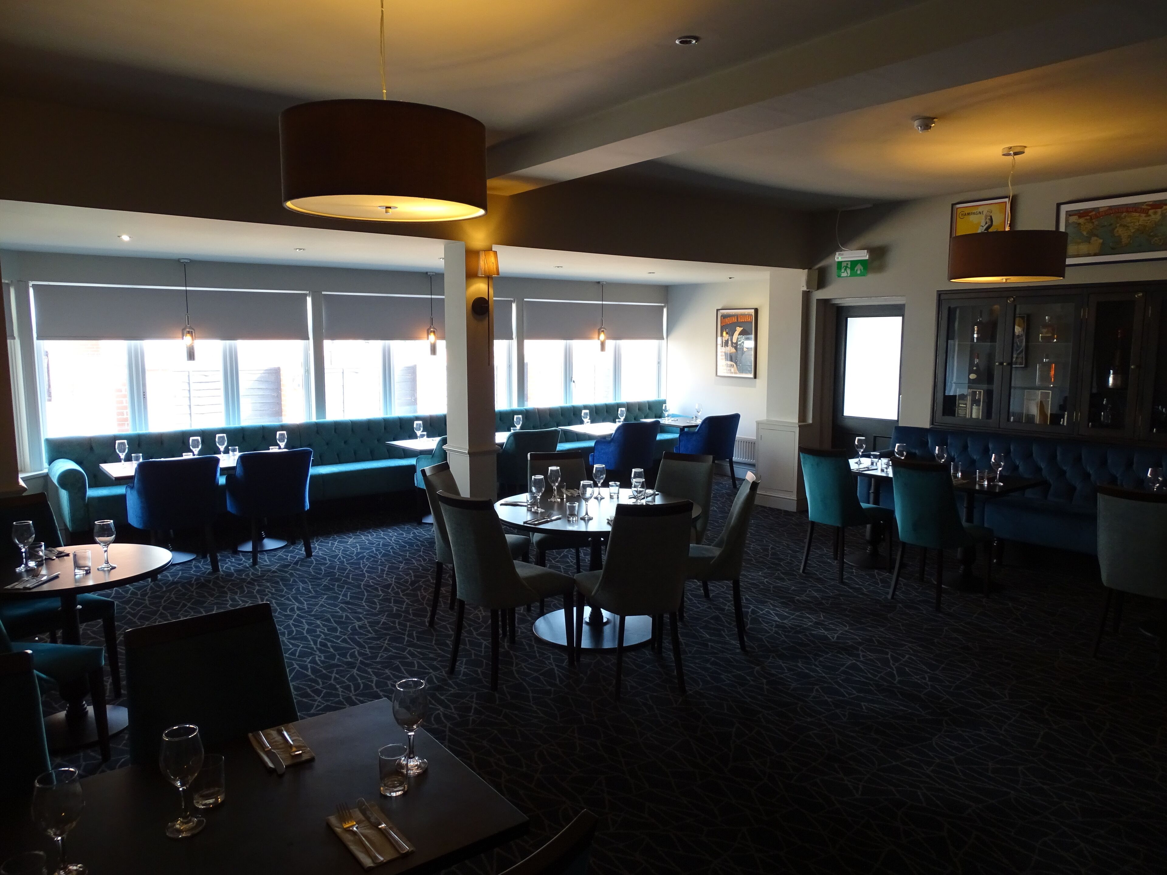 Ein Restaurant mit blauen Sitzbänken, runden Tischen und Pendelleuchten.