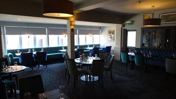A restaurant with blue upholstered booths, round tables, and pendant lighting.