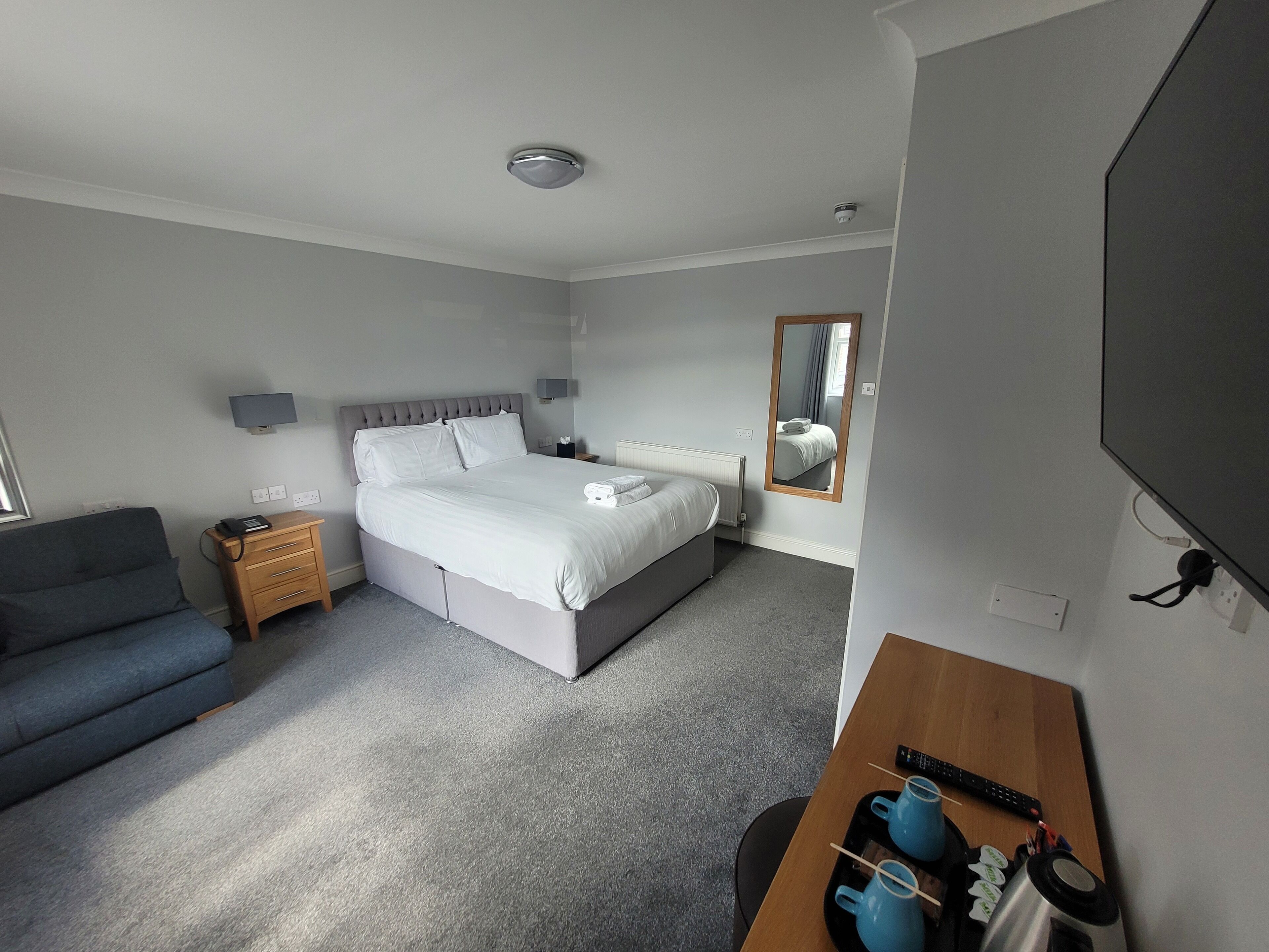 Habitación de hotel con cama, mesita de noche, lámpara y escritorio con silla.