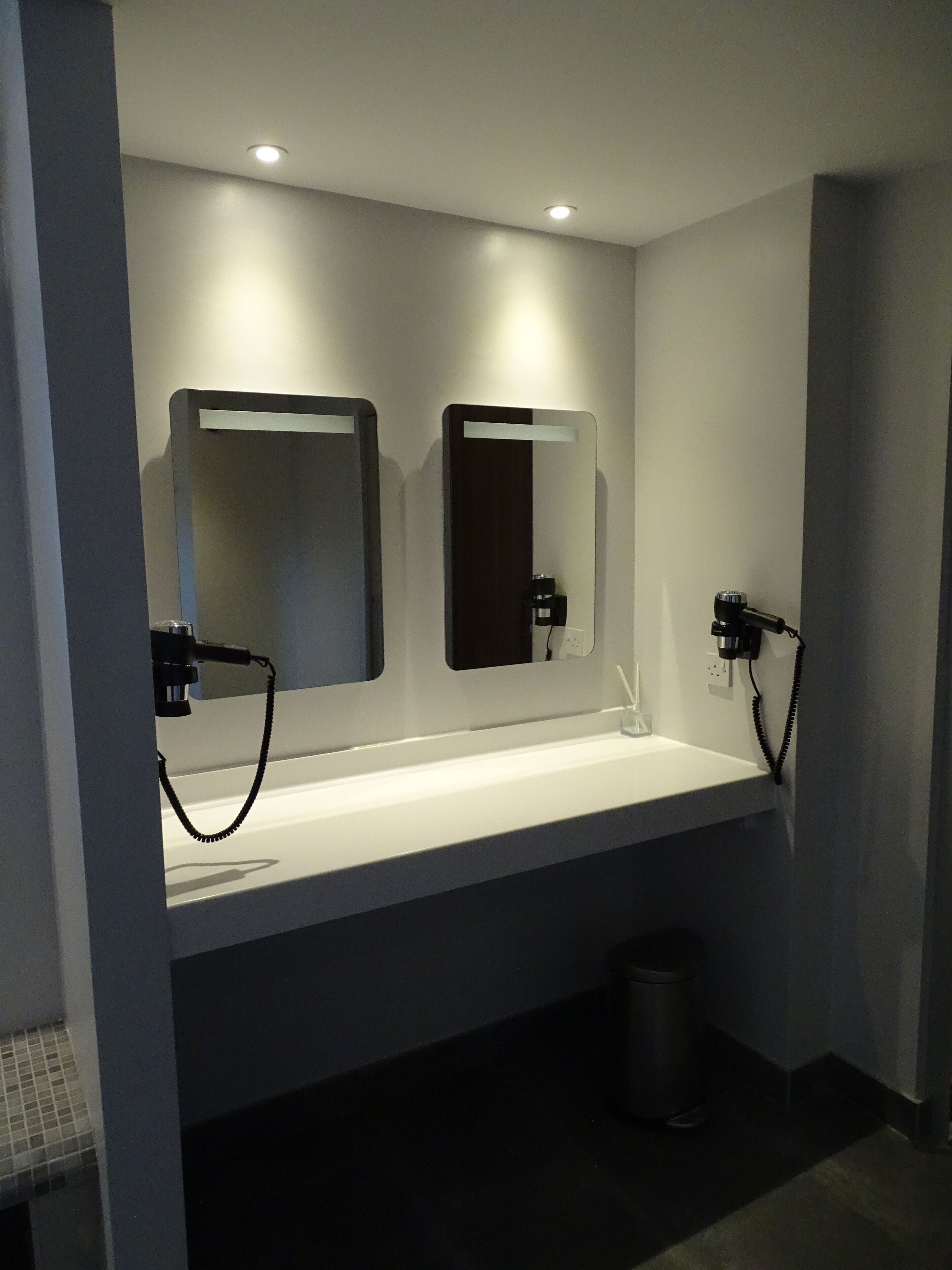 A modern bathroom with a white sink, two mirrors, and a hairdryer.