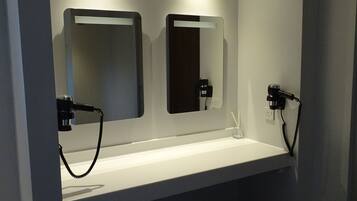 A modern bathroom with a white sink, two mirrors, and a hairdryer.
