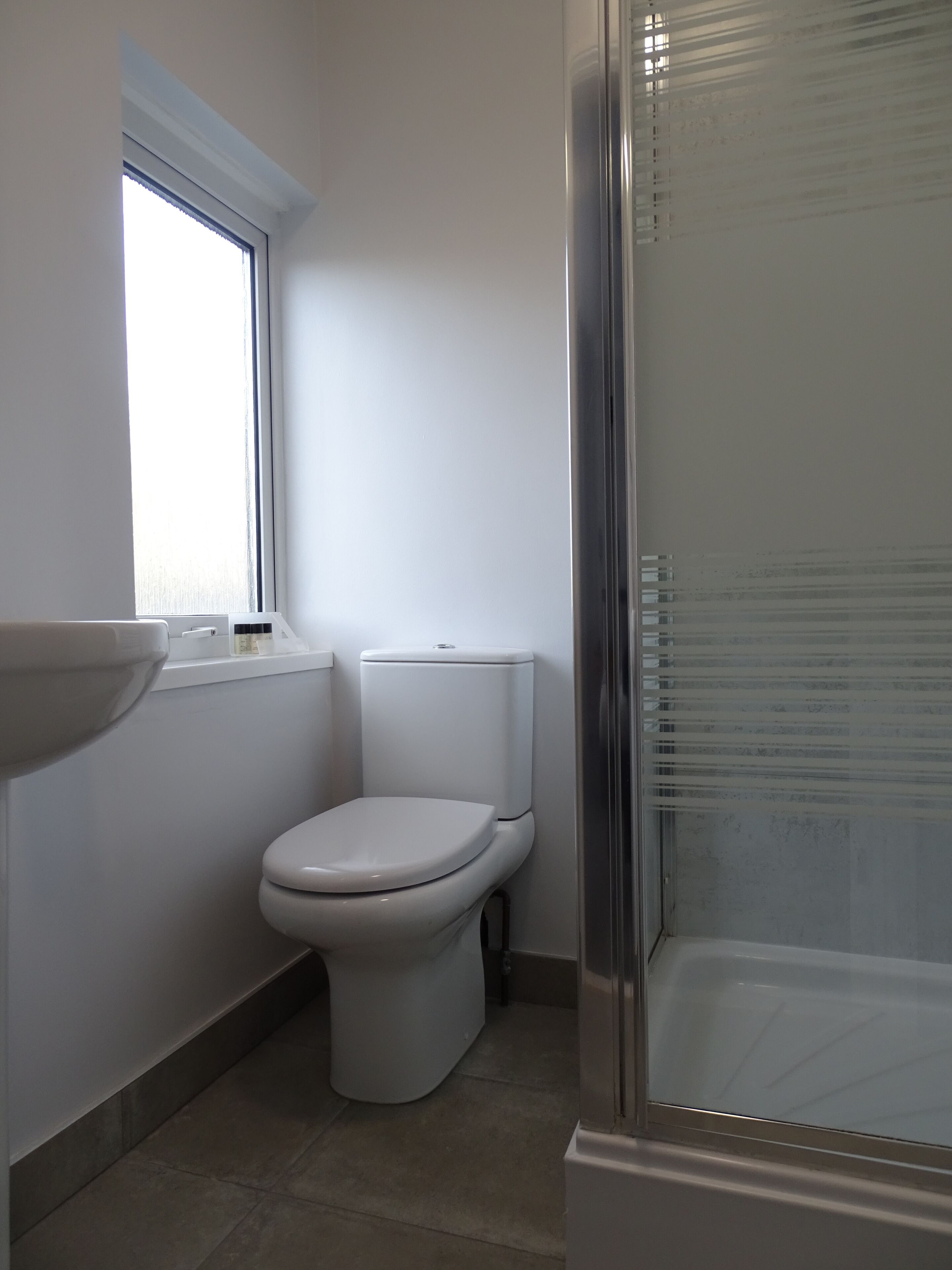A bathroom with a toilet, a window, and a shower.
