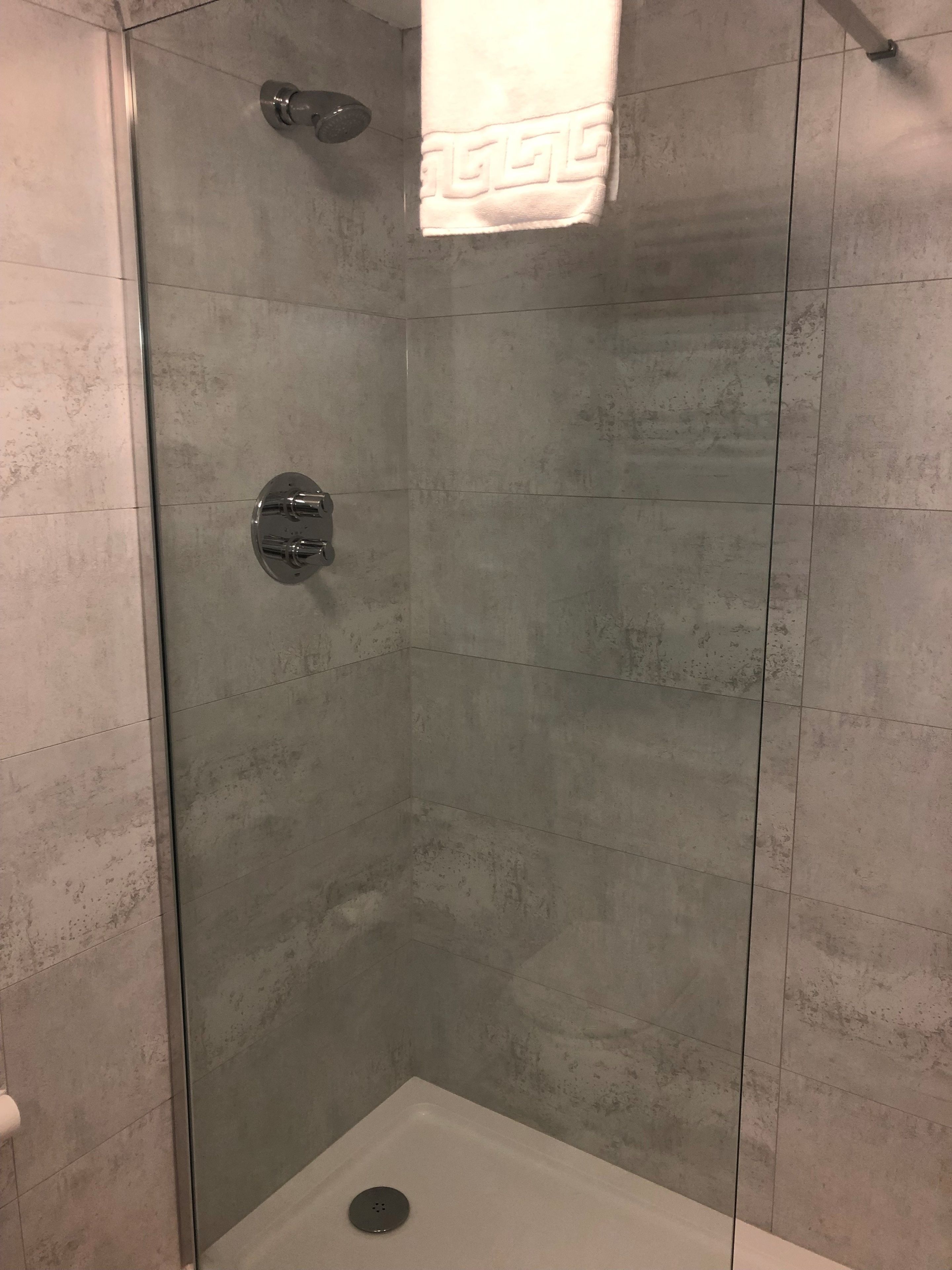 A glass-enclosed shower stall with a white towel hanging on the wall.