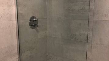 A glass-enclosed shower stall with a white towel hanging on the wall.
